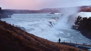 İzlanda 'da Gullfoss şelalesinin yanında duran turist figürlü statik manzara, kar ve buzla kaplanmış muhteşem bir kış şelalesi. Yavaş çekim