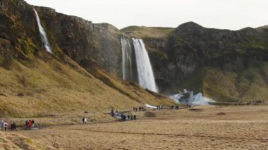 Turist grupları, ilkbaharda Seljalandsfoss 'un güzel şelalesinin oradaki patikalarda yürürler.