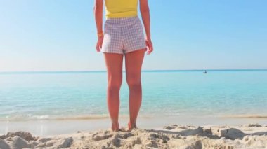 Kıbrıs 'ın Nissi plajında duran güzel genç kadın yaz tatilinde açık havada deniz manzarasının keyfini çıkarıyor. Mavi gökyüzü ve berrak Akdeniz sularıyla beyaz kumsal