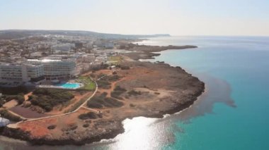 Ayia Napa, Kıbrıs - 15 Nisan 2023: Kıbrıs Rum Kesimi tarafındaki Ayia Napa körfezi üzerinde turkuaz plajlar ve otel tatil beldeleri ile kuş bakışı uçuş. Ünlü tatil beldesi