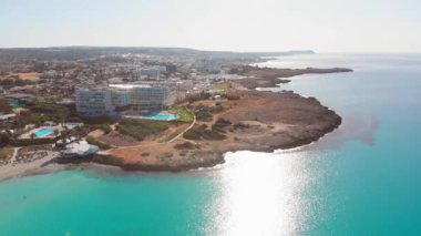 Ayia Napa, Kıbrıs - 15 Nisan 2023: Kuşlar, Kıbrıs Rum tarafındaki Ayia Napa körfezine turkuaz plajlar ve otel tatil beldeleri panoramasıyla bakıyor. Ünlü tatil beldesi.