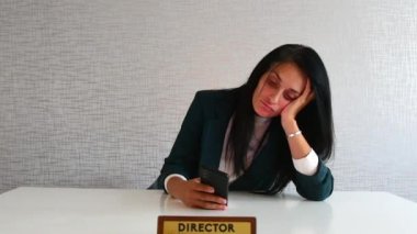 Genç Kafkasyalı esmer iş kadını direktör masasında oturuyor telefon tomarı haber sosyal medyasını kullanıyor iş yönetmeninden sıkılıyor. Gereksiz bir ofis şakası.