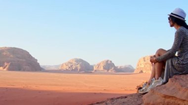 Wadi Rum Çölü 'nde, gün batımında uçurumun kenarında oturan kadın turist Wadi Saabit vadisinde. Jordan kavramı keşfet
