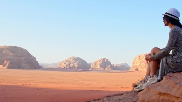 ドレスの女性観光客は ワディ ラム砂漠の日没の視点で崖の上に座る 谷ワディ サバト ヨルダン コンセプトを探る — ストック動画