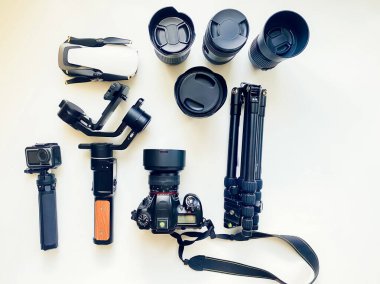 Beyaz masa arkasında profesyonel fotoğrafçı için ekipman bulunan düz kompozisyon. Gimbal, lens, drone, tripod, kamera, aksiyon kamerası modası geçmiş. Metin için izole edilmiş boşluk