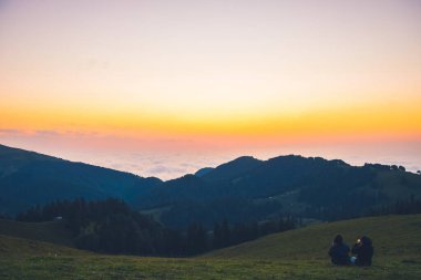 Bakhmaro, Georgia - 6th august, 2022 : Sunset over clouds in georgia caucasus mountains with tourist girl sit enjoy sunset have fun together outdoors on vacation clipart