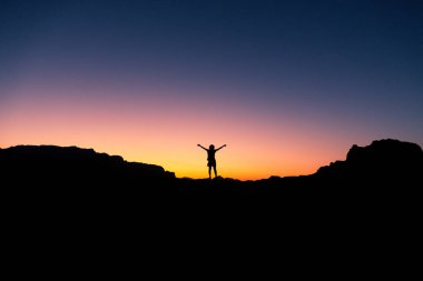 Özgür neşeli kadın yürüyüşçünün silueti Dağın zirvesinde kollarını aç Ürdün 'deki Wadi Rum çölünde gün doğumunu selamla