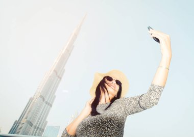 Kafkasyalı genç turist Burj Halife 'nin güneşli gökyüzü gününde akıllı telefonuyla cep telefonunun selfie fotoğrafını çekiyor.