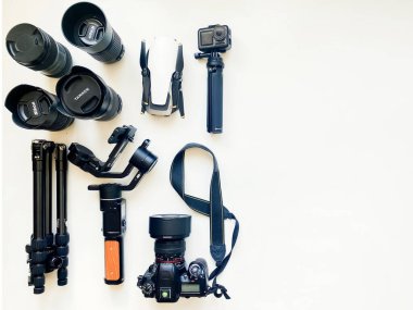 ABD - 2022: Beyaz masa arkasında profesyonel fotoğrafçı için ekipman içeren düz kompozisyon. Gimbal, lens, drone, tripod, kamera, aksiyon kamerası. Metin için izole edilmiş boşluk