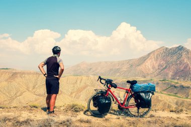Kafkasyalı erkek bisikletçi, kırmızı bisiklet turunda dikilip manzaralı dağ manzarasına bakıyor. Etkin ilham verici yaşam tarzı konsepti
