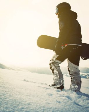 Snowboardcu, gün batımında karlı dağlarda snowboard ile yürüyor. Sinema solo freerider snowboardcusu