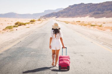 Cinematic travel background young carefree caucasian traveler tourist on road walk drag luggage barefoot to beautiful landscape. Travel concept direction and next trip destination