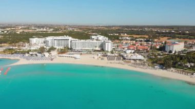Ayia Napa, Kıbrıs - 15 Nisan 2023: Ada yeşili manzaralı plaj kıyısında havuzları olan lüks otel binaları. Nissi Körfezi otoparkında araçlar.