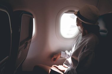 Kadın uçan bir uçağın penceresinden dışarı bakıyor. Genç Kafkas mutlu yolcular uçakla seyahat ediyorlar, gökyüzünü yukarıdan izliyorlar ve pasaportlarını tutuyorlar.