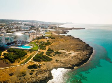 Ayia Napa, Kıbrıs - 15 Nisan 2023: Kıbrıs Rum Kesimi tarafındaki Ayia Napa körfezi üzerinde turkuaz plajlar ve otel tatil beldeleri ile kuş bakışı uçuş. Ünlü tatil beldesi