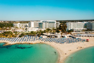 Ayia Napa, Cyprus - 15th april, 2023: aerial fly over Luxury hotel buildings with pools by beach with island greenery panorama.White sand most famous in Cyprus - Nissi beach clipart