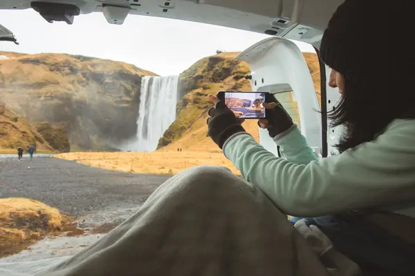 stock image Traveler woman shoot video photo of beautiful waterfall use smartphone. Female tourist is taking photo with mobile phone camera while travel in Iceland stay in campervan by Skogafoss