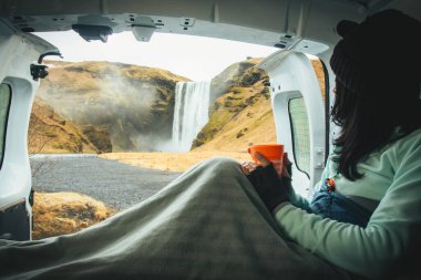 Turist kadın gezgin Skogafoss 'un kiralık karavanın içindeki açık kapılı manzarasının tadını çıkarıyor. Skogafoss Şelalesi, İzlanda. Tek başına İzlanda 'yı gezmek. Resmi kamp alanı olarak kalın.