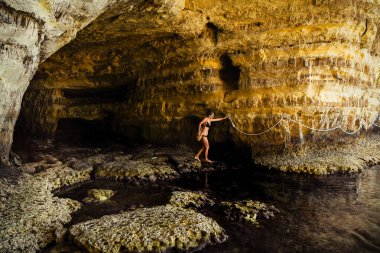 Kadın turist Ayia Napa Körfezi 'ndeki mağaraları keşfediyor. Güzel kayalık deniz mağaraları. İpli gezi yolu. Doku ve adaların jeolojisi.