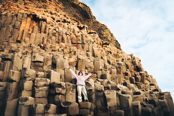 stock image Iceland tourist at beach standing on basalt columns spread hands up on Reynisfjara beach, the black sand beach of Vik, South Iceland coast. Happy woman visiting tourist attraction