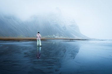 Kadın gezgin solitaire, volkanik siyah kum üzerinde özgürlüğü hissediyor. Stoksnes, İzlanda 'da mor ceketli mutlu bir kız. İzlanda 'da ünlü bir yer. Vestrahorn.