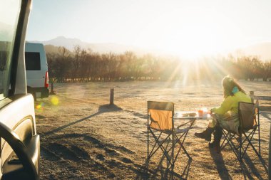 Katlanabilir sandalyede oturan kadın turist, yaz aylarında İzlanda 'daki resmi Skogafoss kamp alanında güneşin doğuşunda kahvaltı yemeğinin tadını çıkarıyor. İzlanda seyahati İskandinavya kavramı