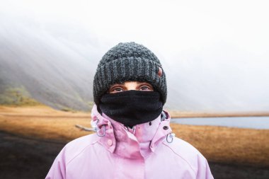Close up caucasian woman with dark eyes in warm clothes stand look at camera. Visit Iceland tourist attractions in harsh icelandic weather conditions clipart