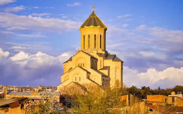 Tiflis 'teki ortodoks kutsal üçleme kilisesi. Eski evler ve çiçek açan bahar ağaçları. Gürcülerin dini ve kültürü. Sakartvelo