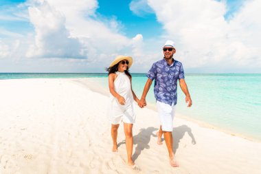 Genç kaygısız beyaz kadın ve erkek, Fulidhoo Adası 'nda balayında tropik beyaz kumsalda yürürken el ele tutuşup gülüyorlar. Maldivler tatil konsepti
