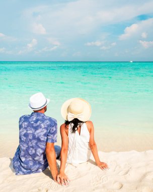 Maldivler 'de tropikal bir plajda beyaz bir çift ufuk ötesindeki okyanus manzaralı tekneyi izliyor.