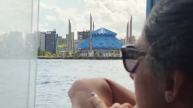 Erkek, Maldivler - 14 Mayıs 2024: Kafkas kadın turist Maldivler adasına giden bir teknede oturuyor ve başkent sahili panoramasının ve Kral Salman camisinin tadını çıkarıyor.