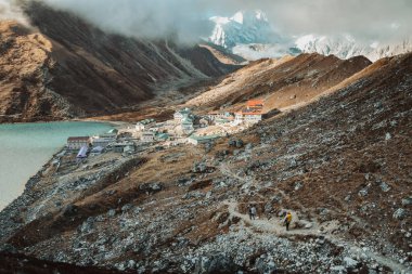 Himalayalar 'da yürüyüş yapan iki yürüyüşçü Gokyo Ri köyüne varır. Nepalli erkek rehber Sagarmatha Ulusal Parkı resmi yürüyüşünde turist müşterisine öncülük ediyor