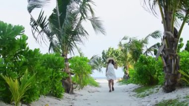 Genç Kafkasyalı kaygısız kadın plaj yolunda yürüyor. Modern turist blogcusu nüfuzunu artıran kişi, Maldivler konseptindeki tatil beldeleri olan tropikal adalardan kaçma modasını teşvik ediyor