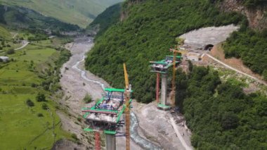Kazbegi, Gürcistan - 7 Temmuz 2024: Çinli inşaatçılar tarafından inşa edilen yeni otoyol projesinin inşaat sahasında havadan görüş vinçleri ve köprü temel direkleri. Çığ baypas tüneli. Tbillisi - Lars