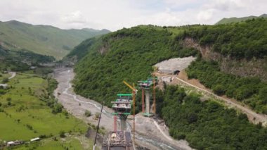 Kazbegi, Gürcistan - 7 Temmuz 2024: Çinli inşaatçılar tarafından inşa edilen yeni otoyol projesinin inşaat sahasında havadan görüş vinçleri ve köprü temel direkleri. Çığ baypas tüneli. Tbillisi - Lars