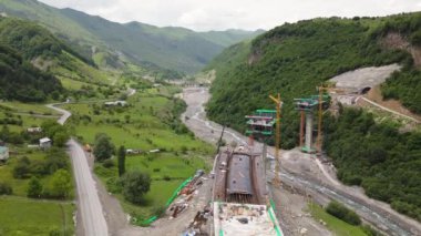 Kazbegi, Gürcistan - 7 Temmuz 2024: Çinli inşaatçılar tarafından inşa edilen yeni otoyol projesinin inşaat sahasında havadan görüş vinçleri ve köprü temel direkleri. Çığ baypas tüneli. Tbillisi - Lars