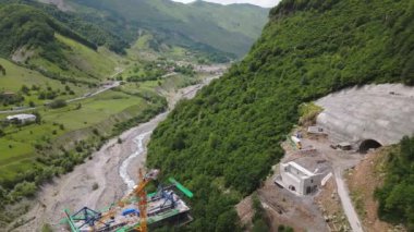 Kazbegi, Gürcistan - 7 Temmuz 2024: Çinli inşaatçılar tarafından inşa edilen yeni otoyol projesinin inşaat sahasında havadan görüş vinçleri ve köprü temel direkleri. Çığ baypas tüneli. Tbillisi - Lars