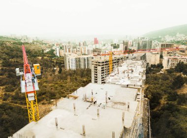 Hava manzaralı inşaat alanı çatıya malzeme yığıyor. Yeşil bölgedeki banliyölerde yüksek binalar var. Tiflis. Gürcistan sonbaharı. Kafkasya dağları emlak yatırımı.