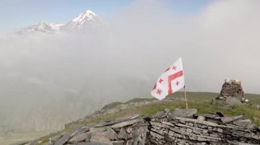 Havadan yükselen Angels Dağı manzaralı Kazbek Dağı tepe arkaplan manzaralı. Kazbegi Ulusal Parkı 'ndaki Gürcistan bayrağı. Gürcistan 'da gizli mücevher yolu yürüyüşü