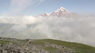 Havadan takip eden beyaz kadın yürüyüşçü. Sırt çantasıyla dağlarda yürüyüş yapan yürüyüşçü. En üst görüş açısına ulaşıyor. Kazbegi Melekleri 'nin dağ yürüyüşü rotasında ilham verici dağlar.