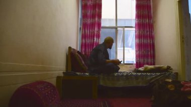 Beyaz, orta yaşlı bir erkek turist, yatakta oturup sosyal medyada Afganistan 'a seyahat deneyimi hakkında bilgi paylaşımı yapıyor. Orta Asya 'da turizm ve seyahat güvenliği