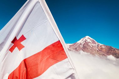 Gürcistan bayrağını Kafkasya dağları ve Kazbek tepe arkaplanı ile kapatın. Seyahat gezisi Gürcistan bayrağını ziyaret et