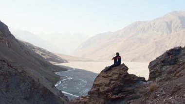 Kafkas erkek yürüyüşçü formda gezgin Pamir dağlarında kayalık bir perspektife oturur vahşi bartang vadisinde manzaranın tadını çıkarır. Tepe zirvelerinde seyahat eder. Spor, turizm ve yürüyüş konsepti. Güneşin doğuşunu izlemek