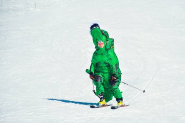 Gudauri, Gürcistan - 15 Şubat 2024: önde kayakçı yeşil dinozor kostümü giyer ve kış tatillerinde kayak merkezinde kayak yaparak eğlenir.