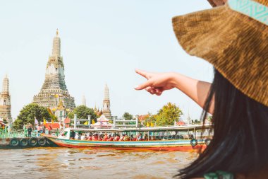 Bangkok, Thailand - 11th february, 2024: caucasian woman tourist point finger to Wat Wrun buddhist temple. Boats dock on pier by famous Siam landmark attraction.Tourist visit historical Thai landmarks clipart