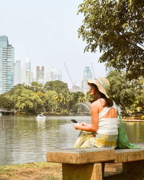 stock image Young tourist woman sit on bench enjoying sunny day visit public Lumpini Park most popular park in Bangkok. Central Business District of Silom