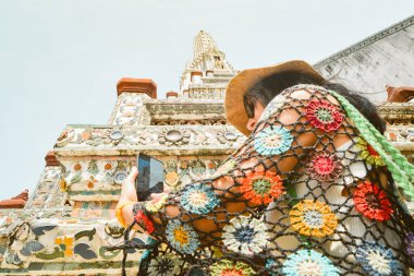 Bangkok, Tayland 'daki güzel Wat Arun tapınağında cep telefonuyla fotoğraf çeken kadın turist. Ünlü turizm merkezi içerik yaratıcısı kavramı sosyal medya sonrası