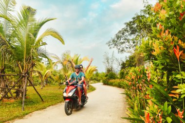 Vietnam 'daki Phu Quoc Adası' ndaki palmiye ağaçlarının altında tropikal tatil sırasında motosikletli scooter kullanan mutlu gezginler.