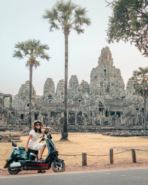 Ünlü Angkor Wat tarihi tapınakları Angkor Thom 'un yanında elektrikli scooterlı mutlu Kafkas turist sürücüsü. Kiralık scooter konseptiyle Güneydoğu Asya 'yı gezin.