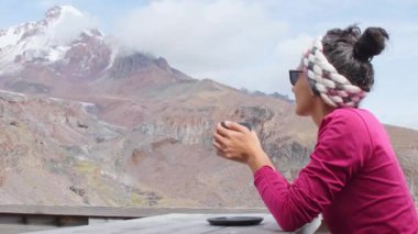 Kafkasyalı genç mutlu turist kadın dağda kafeteryada oturuyor sıcak çikolata içiyor Kazbek dağlarının zirvesini seyrediyor Kazbegi ulusal parkında. Gürcistan 'a sonbaharda seyahat